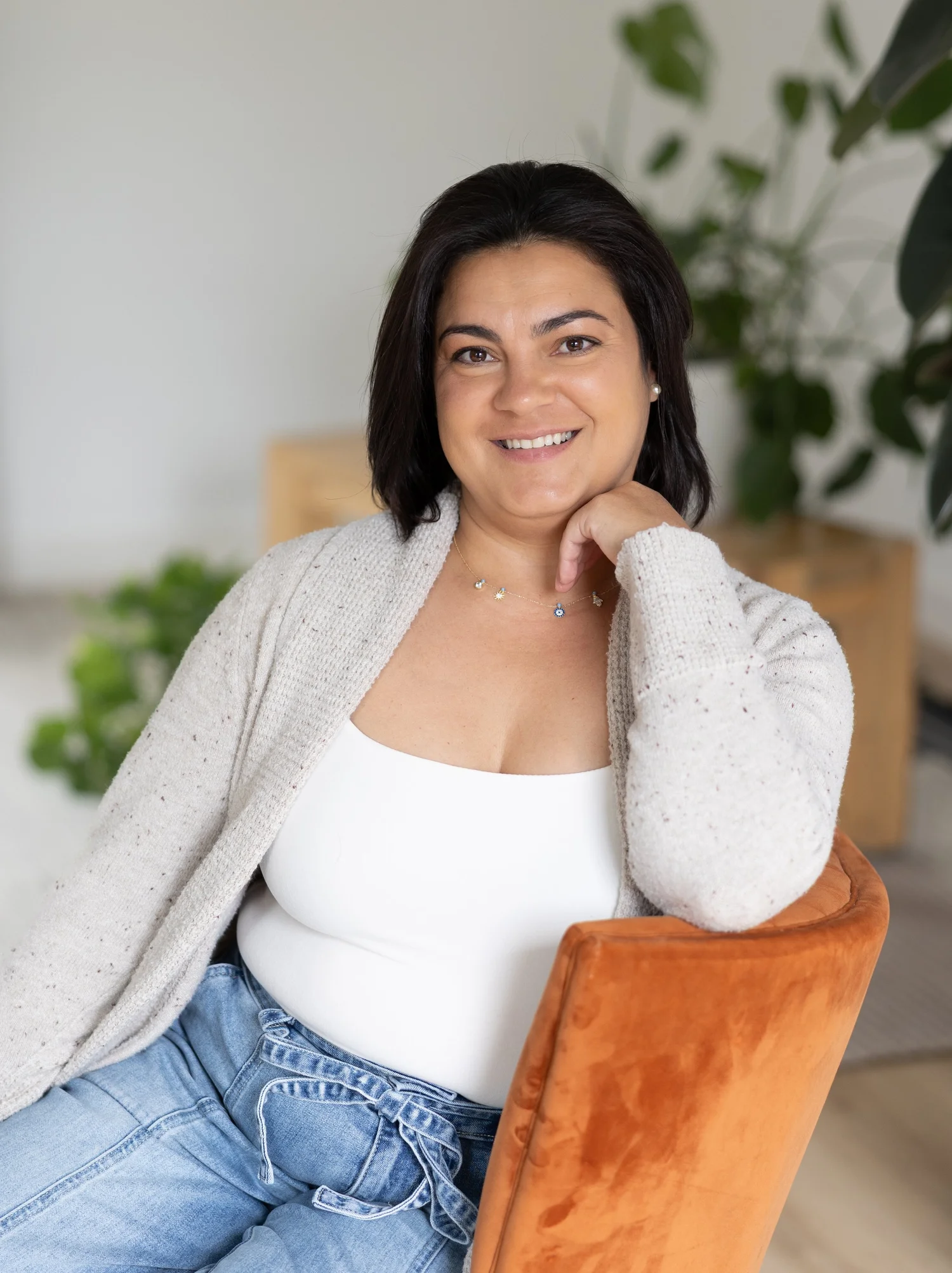 La Dra. Tatiana Turo-Handy sentada en una silla de madera, sonriendo, con plantas verdes al fondo.