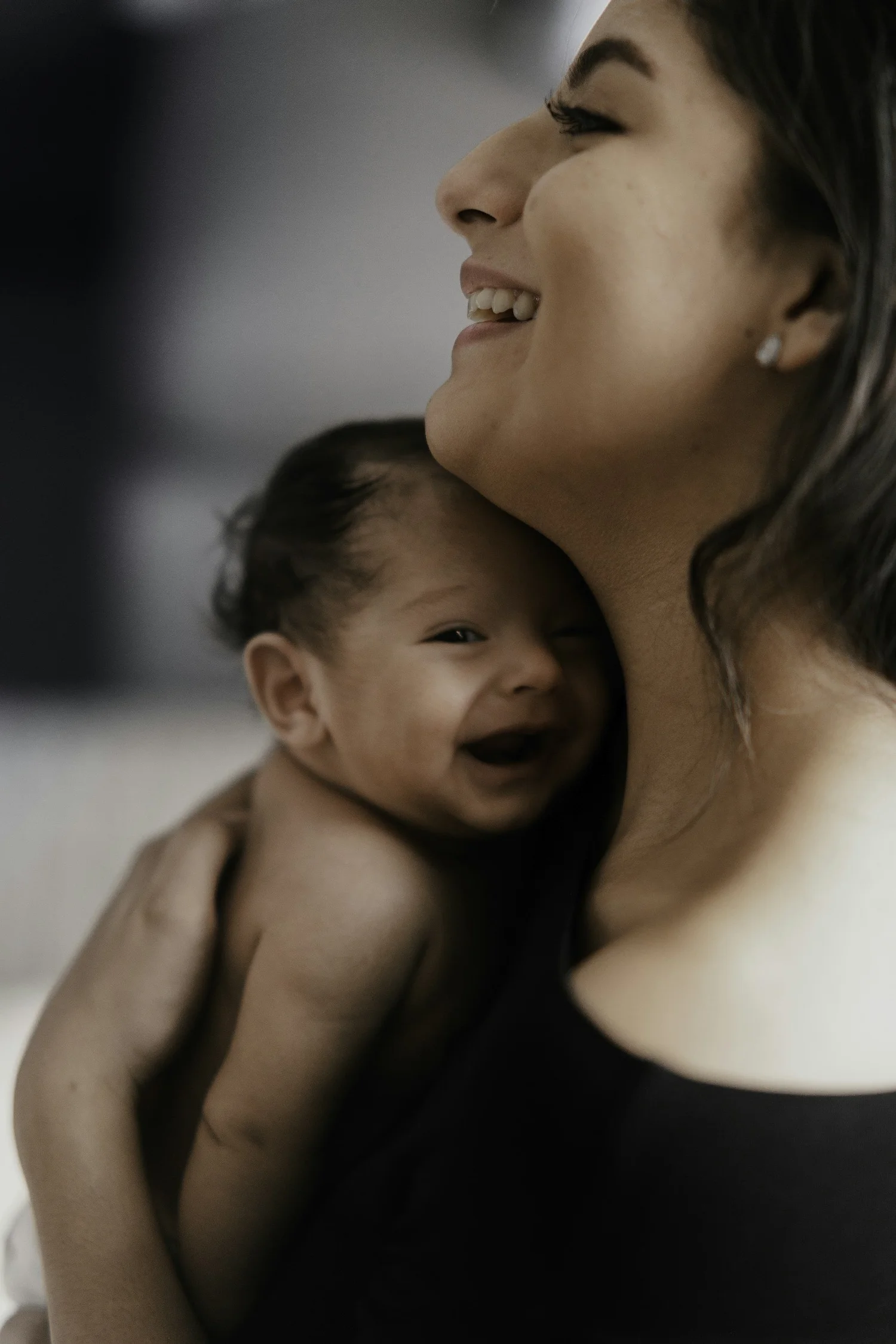 Una mujer sostiene a un bebé sonriente cerca de su pecho; ambos parecen felices.
